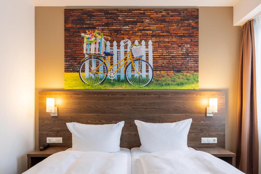 2 Betten in einem Hotelzimmer mit einem Gemälde von zwei Fahrrädern in der Unterkunft Trip Inn Hotel Münster City in Münster