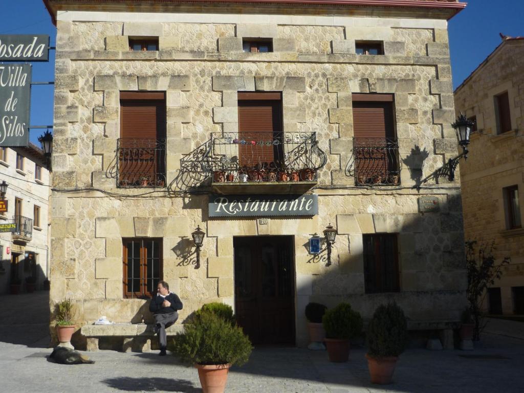 un homme assis sur un banc devant un bâtiment dans l'établissement Hotel Rural Villa de Silos, à Santo Domingo de Silos