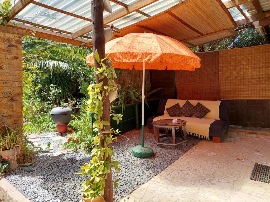 een patio met een parasol en een bank onder een dak bij Santika Garden Cottage Stellenbosch in Stellenbosch