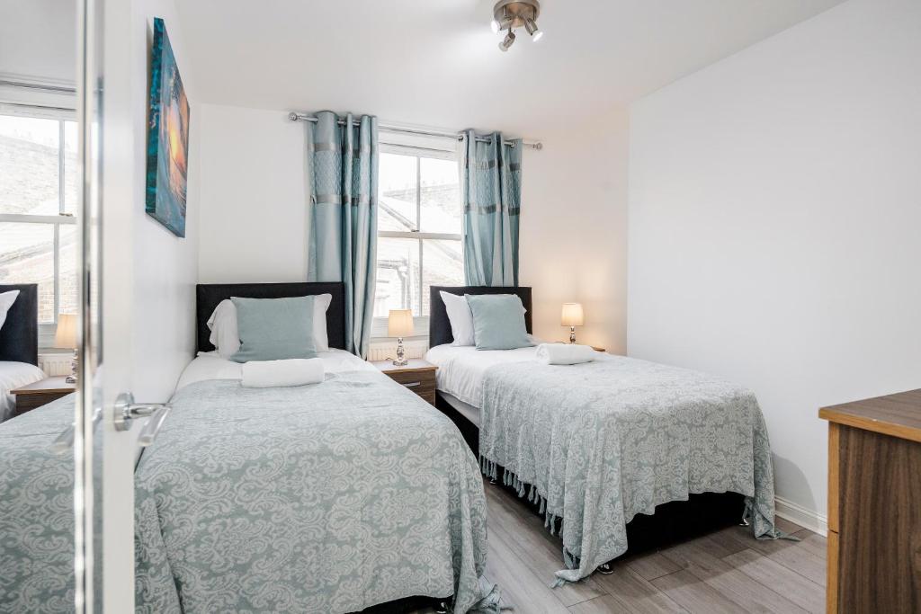 two beds in a bedroom with blue curtains at Beautiful 1-Bed Apartment in London Lewisham in London