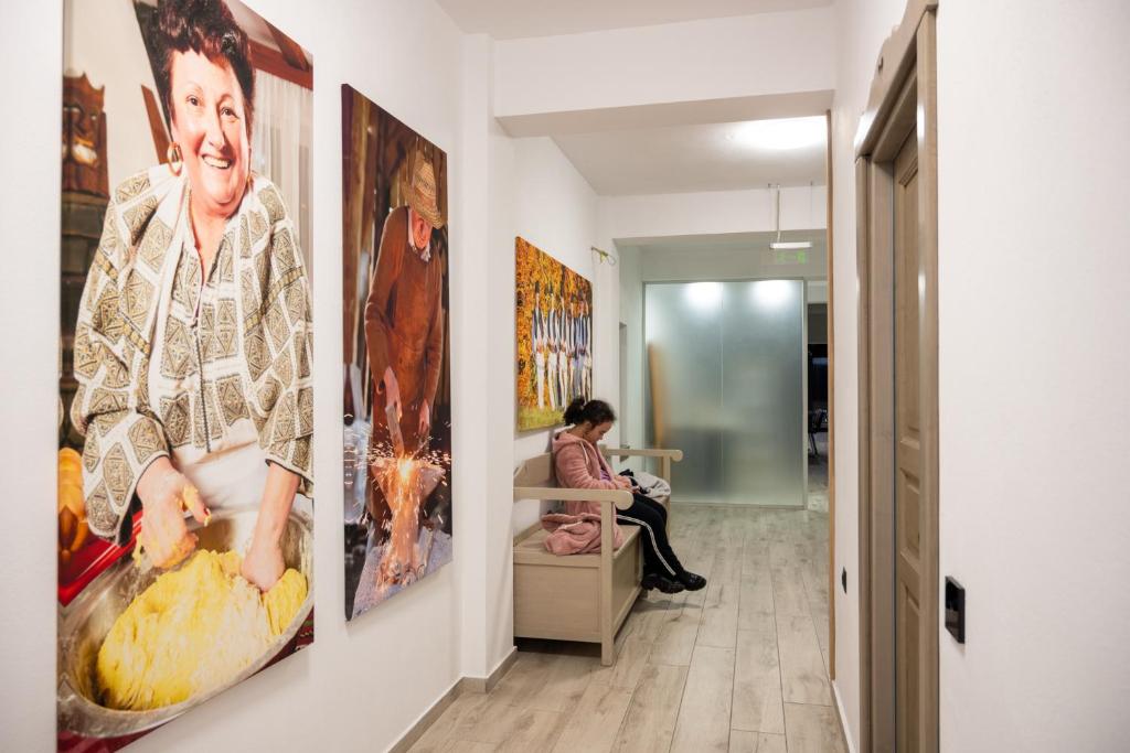 a woman sitting in a chair in a hallway with art on the walls at Pension Mama Cozonacilor in Bran