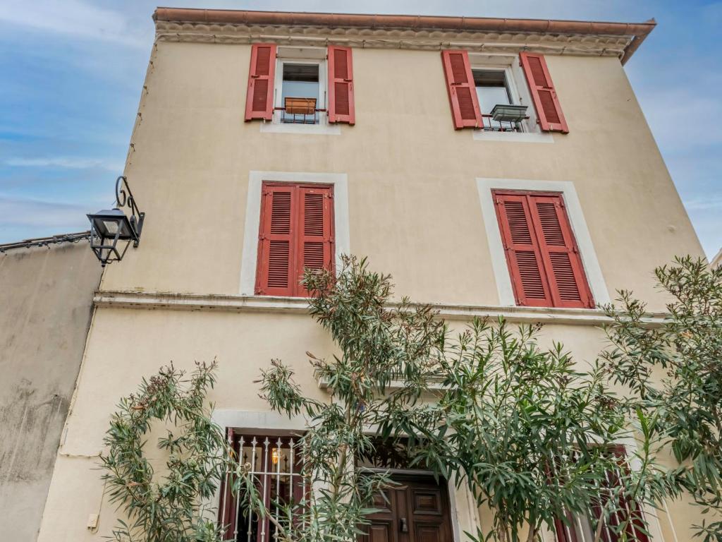a building with red shuttered windows and a tree at Holiday Home La Maison Theaulon by Interhome in Aigues-Mortes