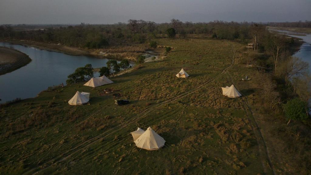 a group of tents on a field next to a river at Burhan Wilderness Camps in Bhurkīā