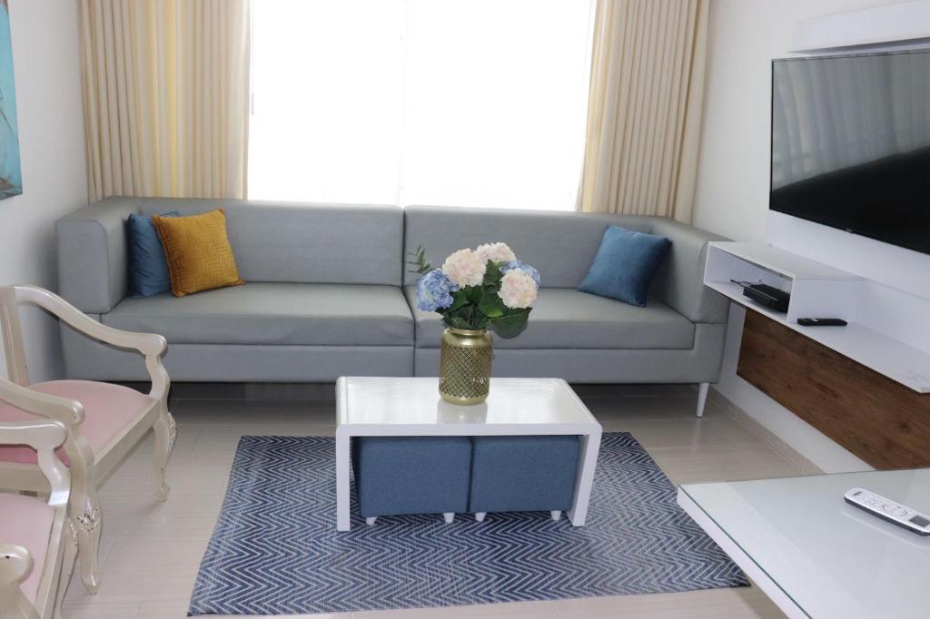una sala de estar con sofá y un jarrón de flores sobre una mesa en Apartamento a 15 min de BUENAVISTA cerca a UNINORTE y CLINICA PORTOAZUL AA 2TV y parqueadero incluido en Barranquilla
