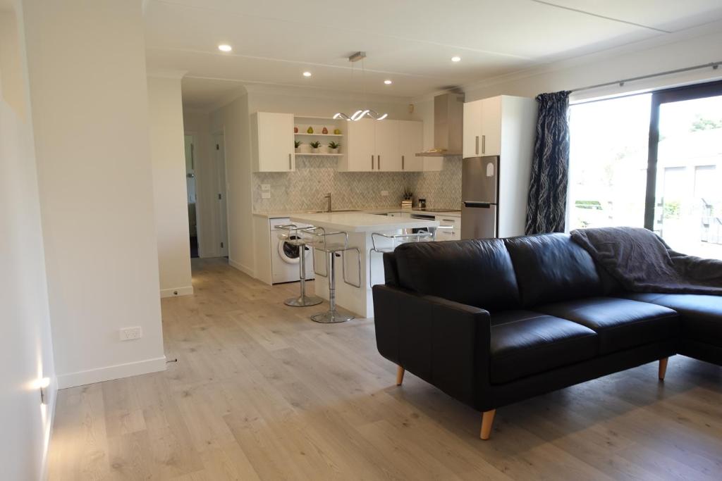 a living room with a black couch and a kitchen at The Guest House in Tamahere