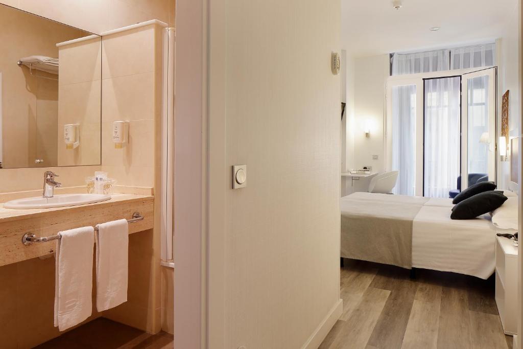 a bathroom with a bed and a sink and a mirror at Hotel Santa Rosa, Blue Hoteles in Gijón