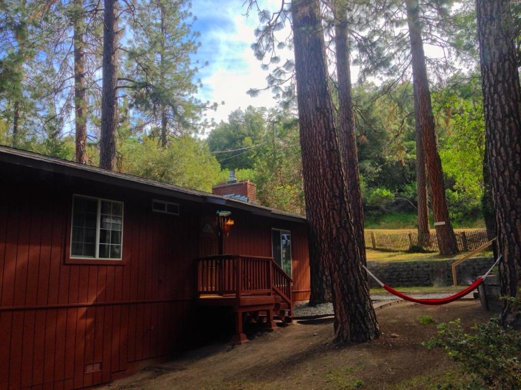 a red cabin in the woods with a tree at Anglers Rest in Oakhurst