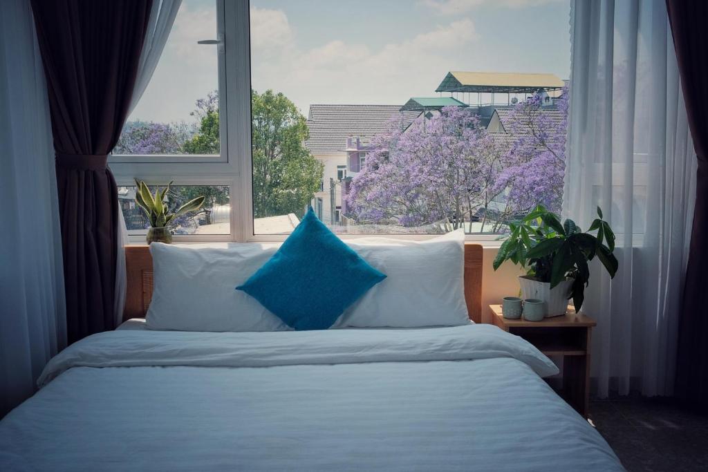 a bed with blue pillows in front of a window at RAON Villa - STAY 24H in Da Lat