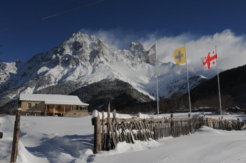 una montaña cubierta de nieve con banderas frente a un edificio en Grand Hotel Ushba en Mazeri