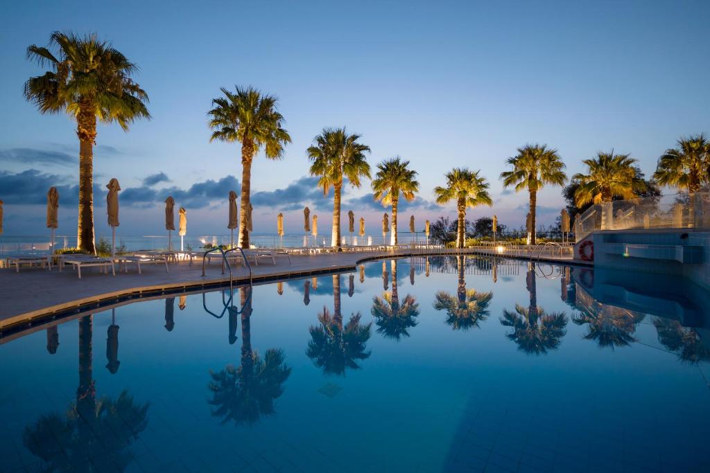 - une piscine avec des palmiers et l'océan dans l'établissement Xenos Kamara Beach, à Argassi