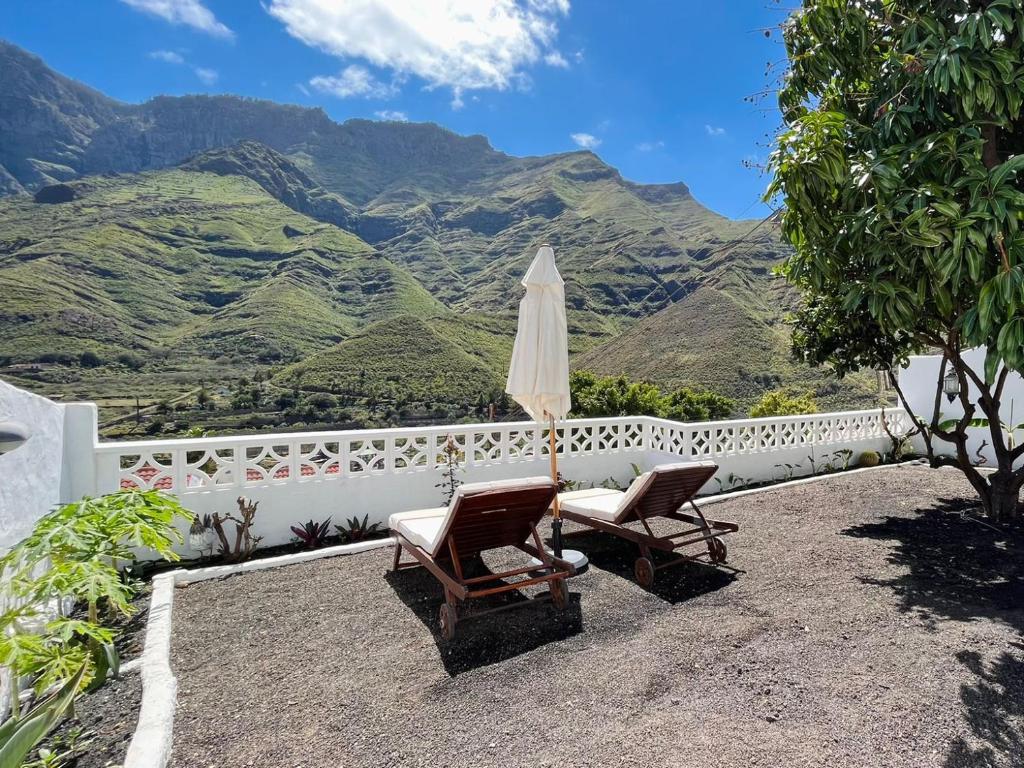 a patio with two chairs and an umbrella and mountains at Jardín de La Suerte in Agaete