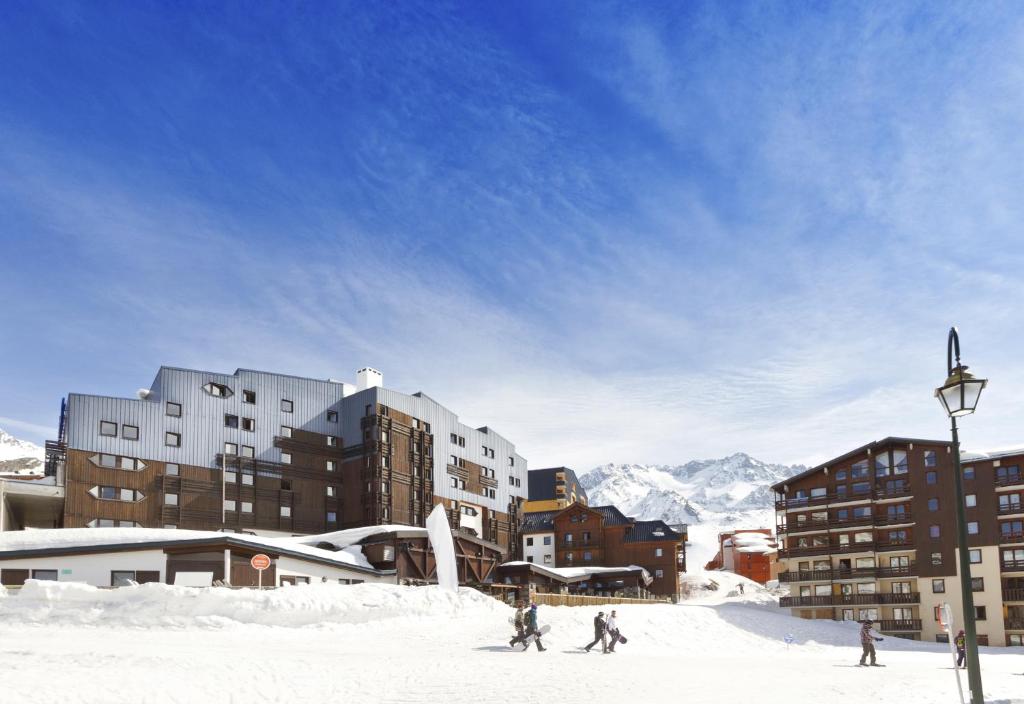 a group of people skiing in the snow in front of buildings at Hôtel Club mmv Les Arolles **** in Val Thorens