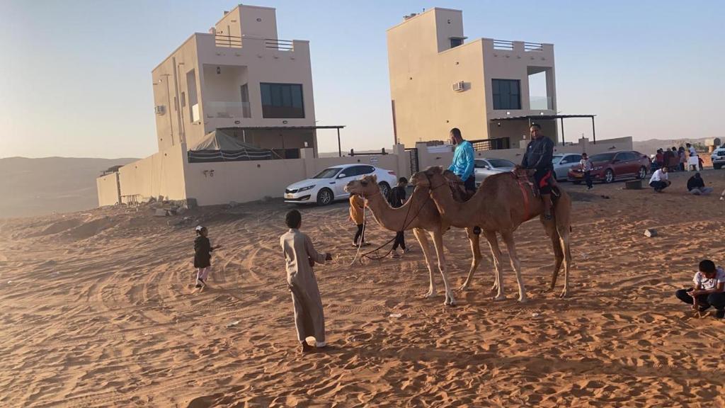 a group of people riding camels in the desert at شاليهات رمال بديه in Al Raka