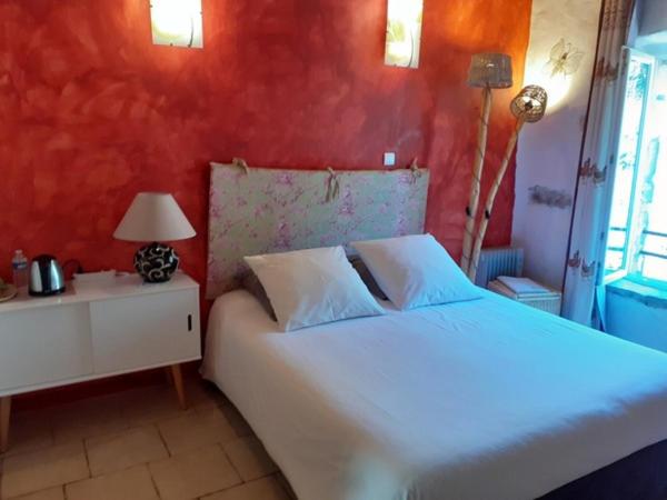 a bedroom with a white bed and a red wall at Au coeur du Caylar in Le Caylar