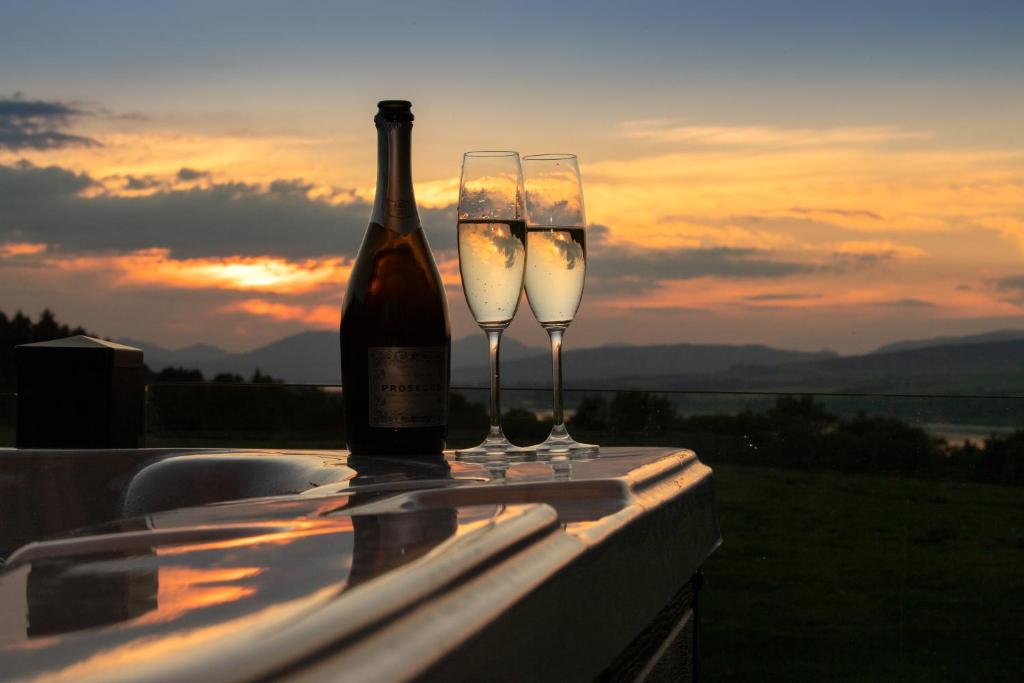 una botella de vino y dos copas en una cornisa en Luxurious Super-king Lodge with hot tub en Langbank