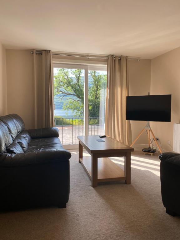 uma sala de estar com um sofá, uma mesa e uma televisão em Borrodale, one bedroom apartment with balcony and loch view. em Fort William