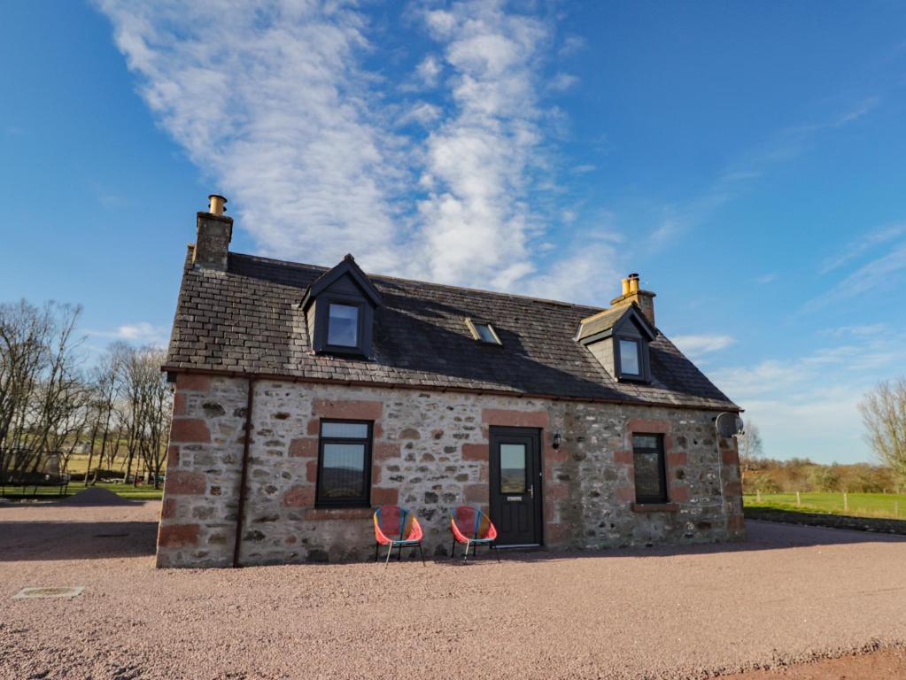 una casa de piedra con dos sillas rojas delante en Nanville en Beauly