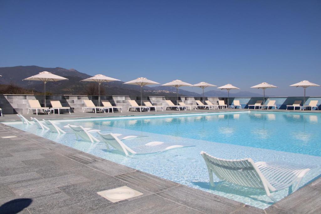 uma piscina com cadeiras brancas e guarda-sóis em hôtel résidence a torra em Vescovato