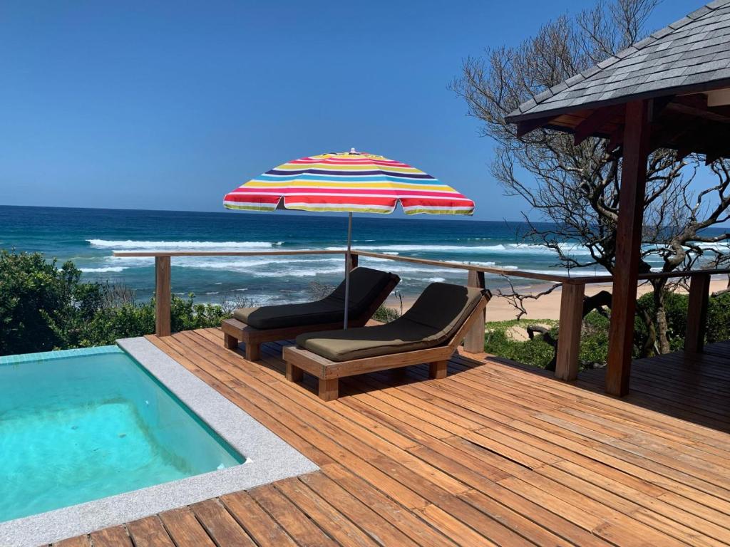 una terraza con 2 sillas y una sombrilla junto a la piscina en Mahi Mahi 3 en Ponta do Ouro