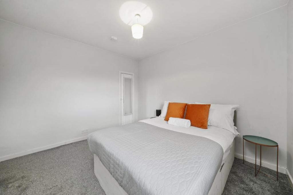Dormitorio blanco con cama blanca y almohadas de color naranja en BridgeCity Hidden Gem of Falkirk, Roughland house, en Carron