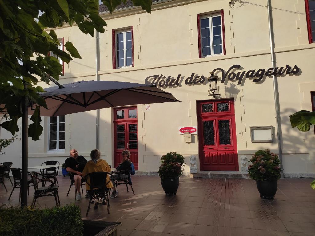 dos personas sentadas en mesas bajo un paraguas frente a un edificio en Hotel des Voyageurs, en Rocamadour