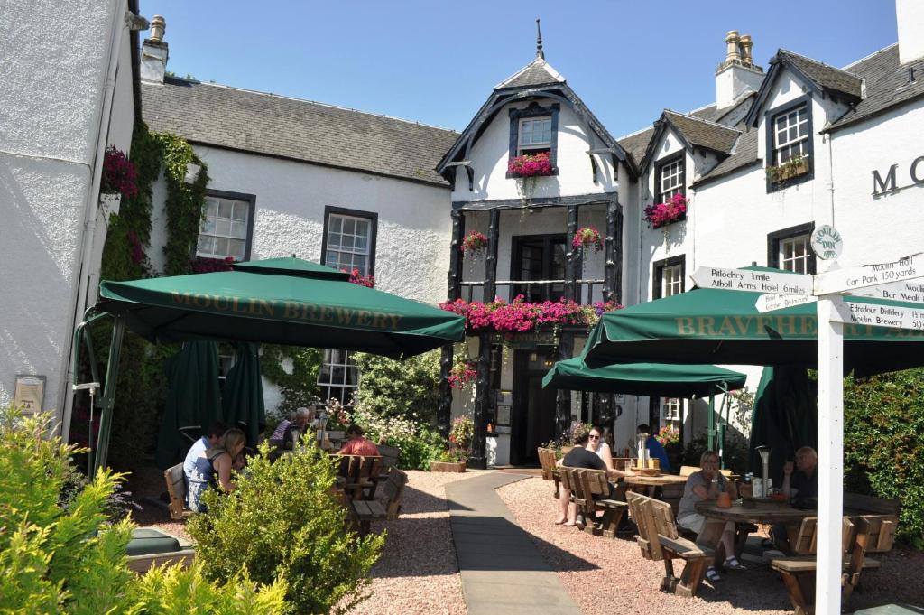 persone sedute ai tavoli e ombrelloni di fronte a un edificio di Moulin Hotel a Pitlochry