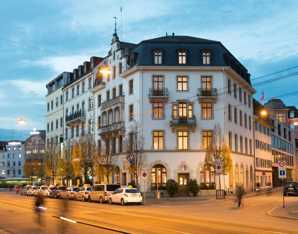 un grand bâtiment blanc avec des voitures garées devant lui dans l'établissement GAIA Hotel Basel - the sustainable 4 star hotel, à Bâle