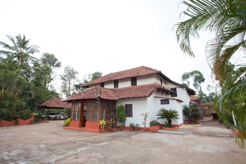 a white house with a palm tree in front of it at Sardar Bahadur's Heritage Bungalow Estate Stay in Napoklu
