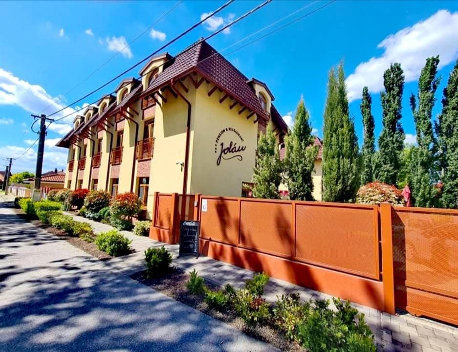un edificio con una valla naranja junto a una calle en Jolán Pension & Restaurant en Číčov