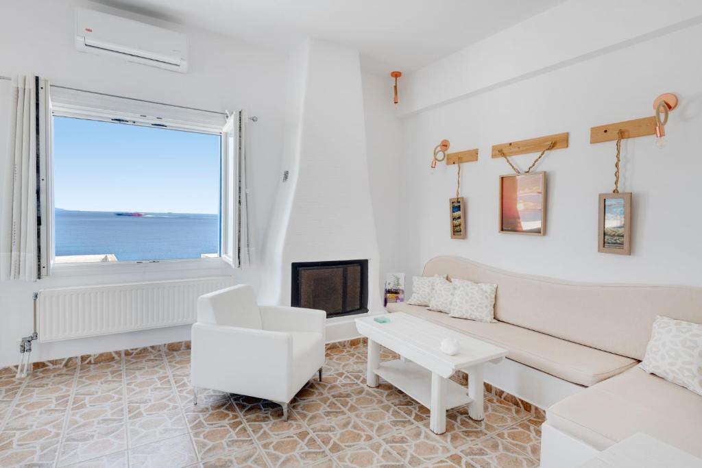Elle comprend un salon doté d'un mobilier blanc et d'une grande fenêtre. dans l'établissement ENDLESS BLUE from Syros - Fabrika Resort, à Vári