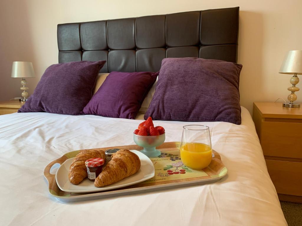 a tray of food on a bed with orange juice and croissants at Portland Mews - 3 Bed Holiday Home By Premier Serviced Accommodation in Leek