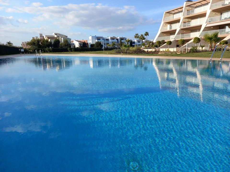 una gran piscina de agua azul frente a un edificio en Prestige & Nature Apartment in Laguna Village, en Quarteira