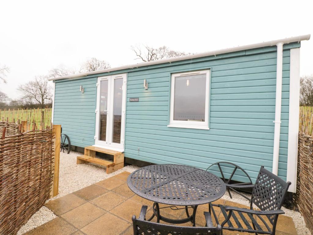 a blue caravan with a table and chairs on a patio at Robins Nest in Southam