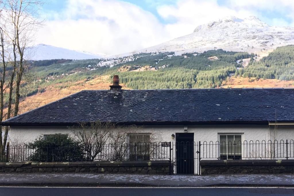 a white house with a fence in front of a mountain at Viking Cottage in Arrochar