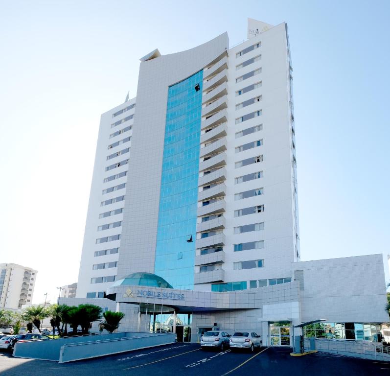 a large white building with cars parked in a parking lot at Nobile Suítes Uberlândia in Uberlândia