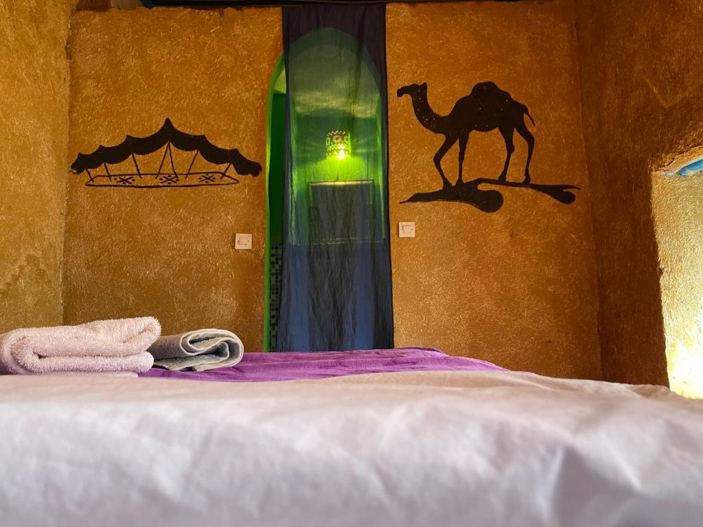 uma cama com uma toalha e um camelo na parede em Dar Yaya em M'hamid