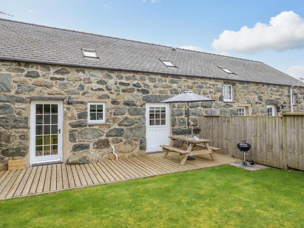 a stone house with a wooden deck with a table and an umbrella at Ysgybor Yd in Chwilog