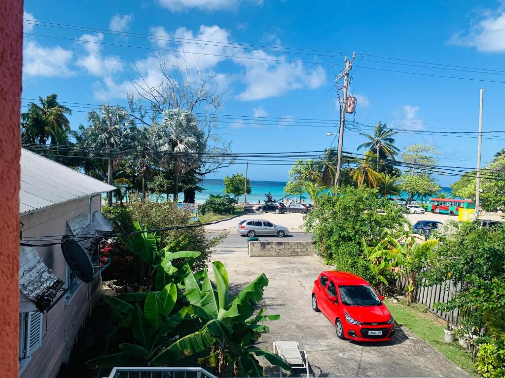 un coche rojo estacionado en un estacionamiento cerca del océano en Ocean View Apartments, en Bridgetown