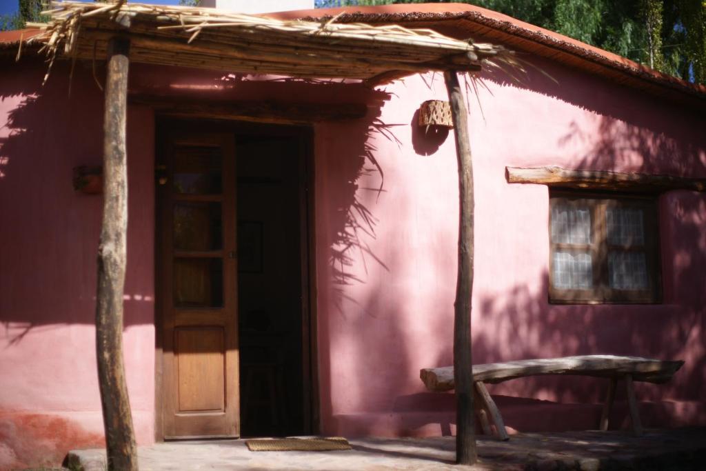 een roze huis met een deur en een bank buiten bij La Calabaza Cabaña in Tilcara