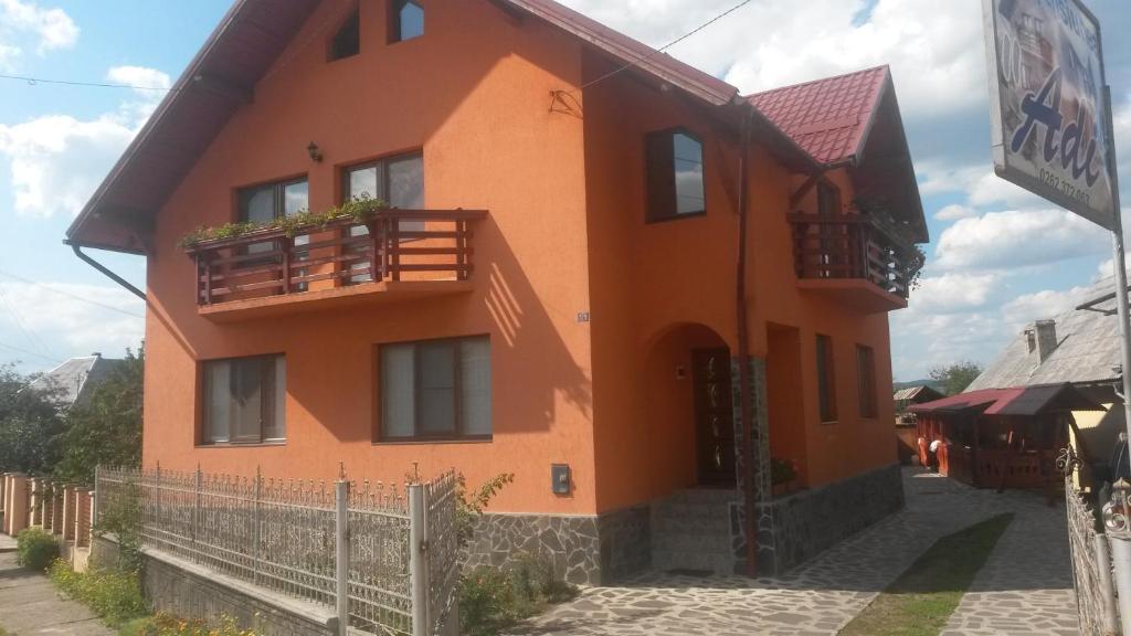 an orange house with a balcony on a street at Pensiunea Adi Sapinta in Săpânța