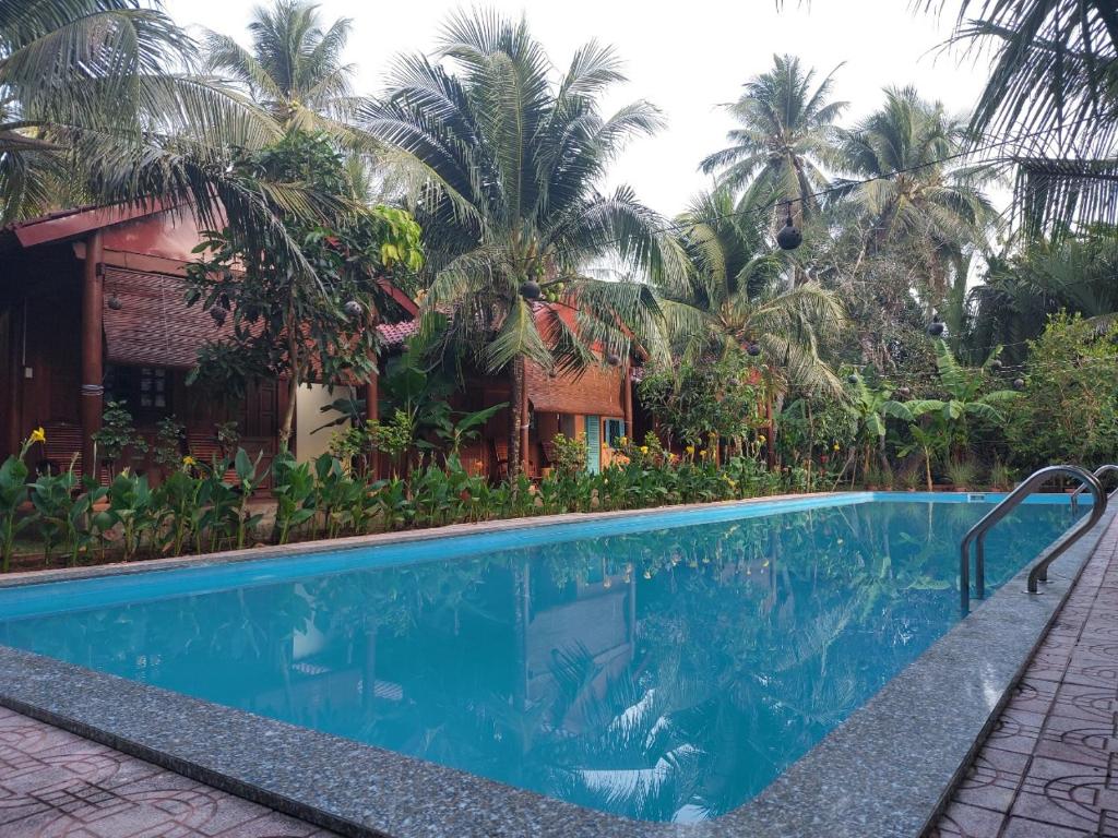 a swimming pool in front of a house with palm trees at Coconut Homestay Mỏ Cày Nam Bến Tre in Ben Tre
