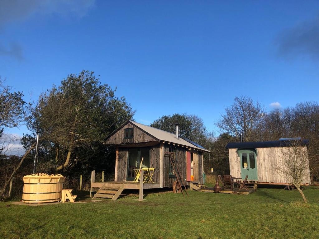 a small house and a shed in a field at Sky View Shepherd's Huts with Woodburning Hot Tub in Redruth