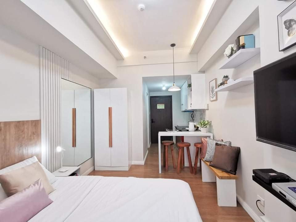 a bedroom with a white bed and a kitchen at SHERISSE' CONDO @ THE LOOP WITH WIFI,CABLE AND HOT & COLD SHOWER, in Cagayan de Oro
