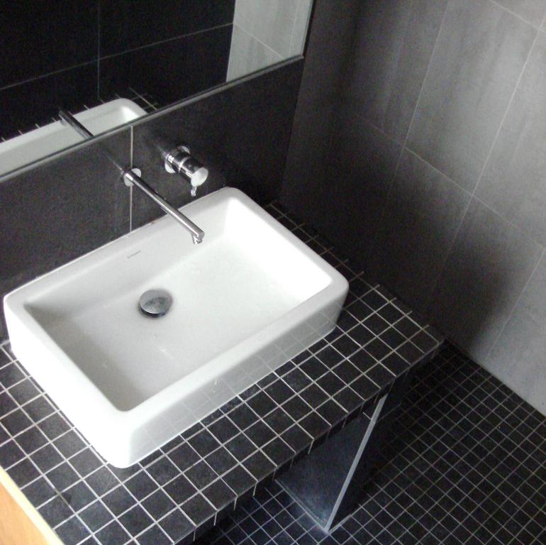 lavabo blanco en un baño de azulejos negros en Plein centre, en París