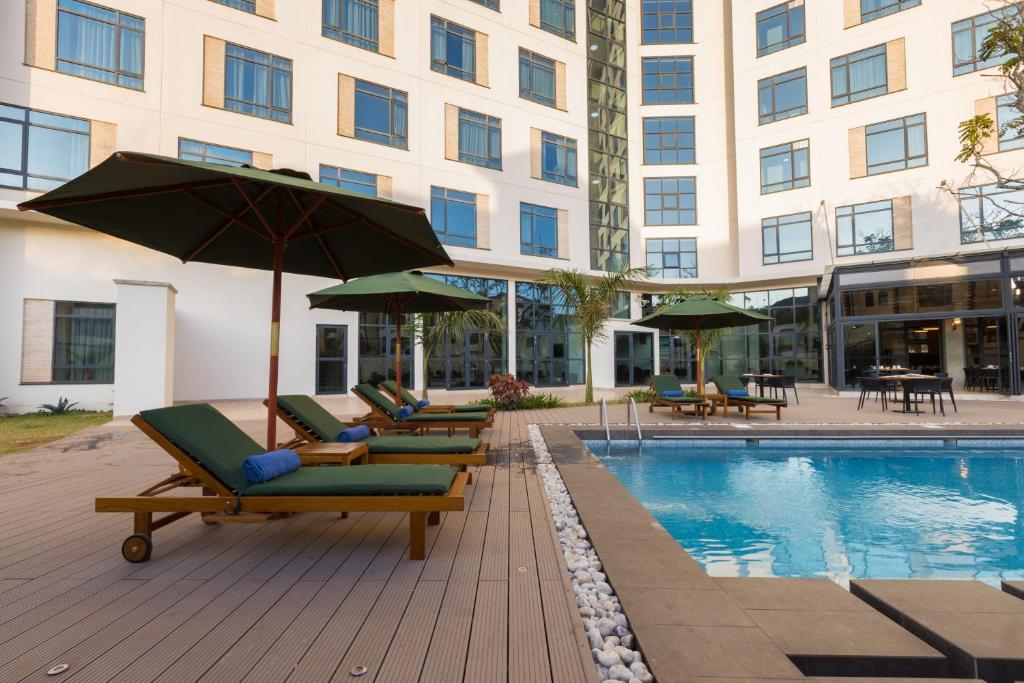 a pool with lounge chairs and umbrellas next to a building at Somerset Westview Nairobi in Nairobi