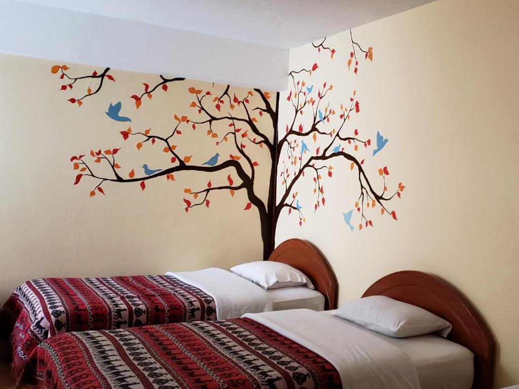 1 dormitorio con 2 camas y un árbol con pájaros en la pared en Nature Home Cusco en Cusco