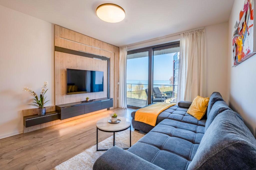 - un salon avec un canapé bleu et une grande fenêtre dans l'établissement MF Coral Beach Apartment, à Siófok