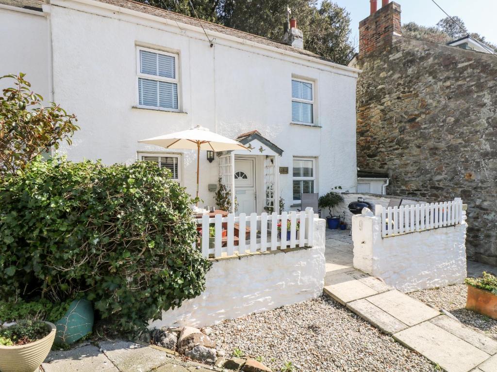 a white house with an umbrella and a fence at Mallards in Pentewan