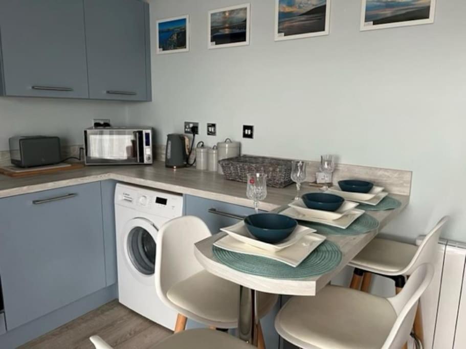 a kitchen with a table and a dishwasher at Orchard Lodge -Coastal Retreat, new build, village views, private garden and terrace in Saint Brides Major