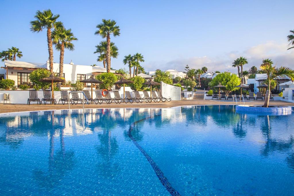 a large blue swimming pool with palm trees and buildings at Jardines del Sol in Playa Blanca